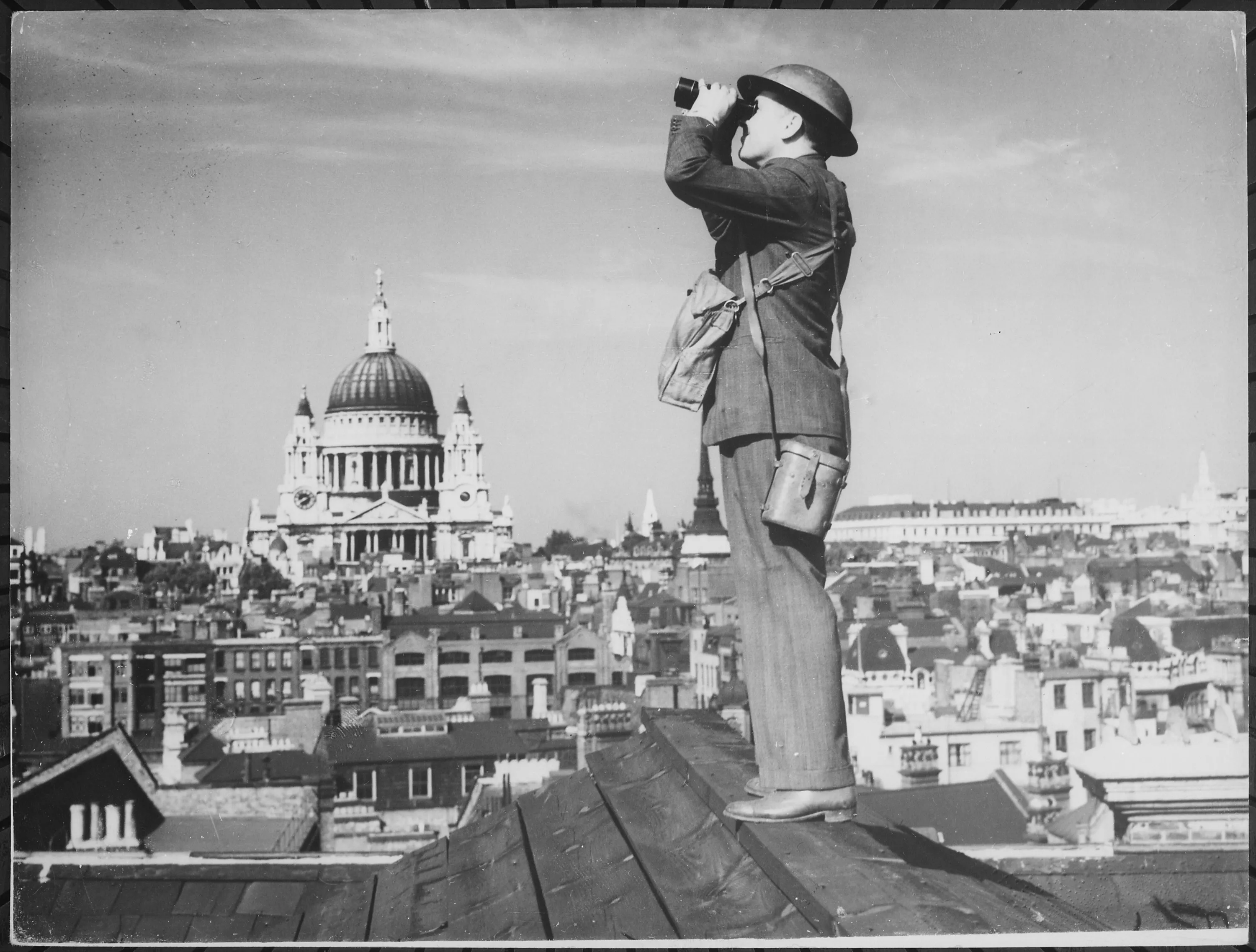 A man in a helmet stands on a London rooftop scanning the sky, with the dome of St Paul's Cathedral behind him
