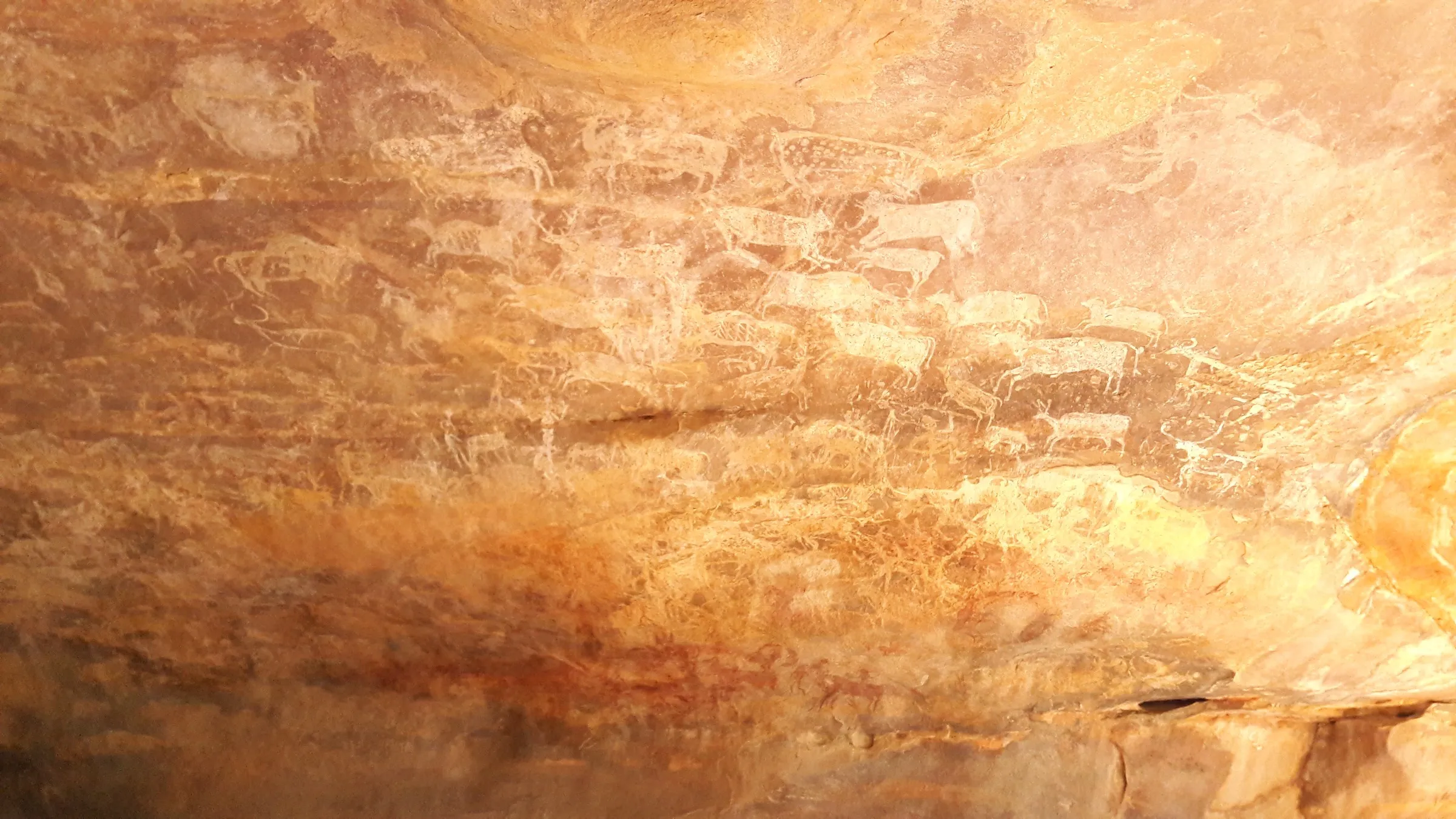 Red ochre rock paintings on a sandstone wall at Bhimbetka, showing human figures and animals