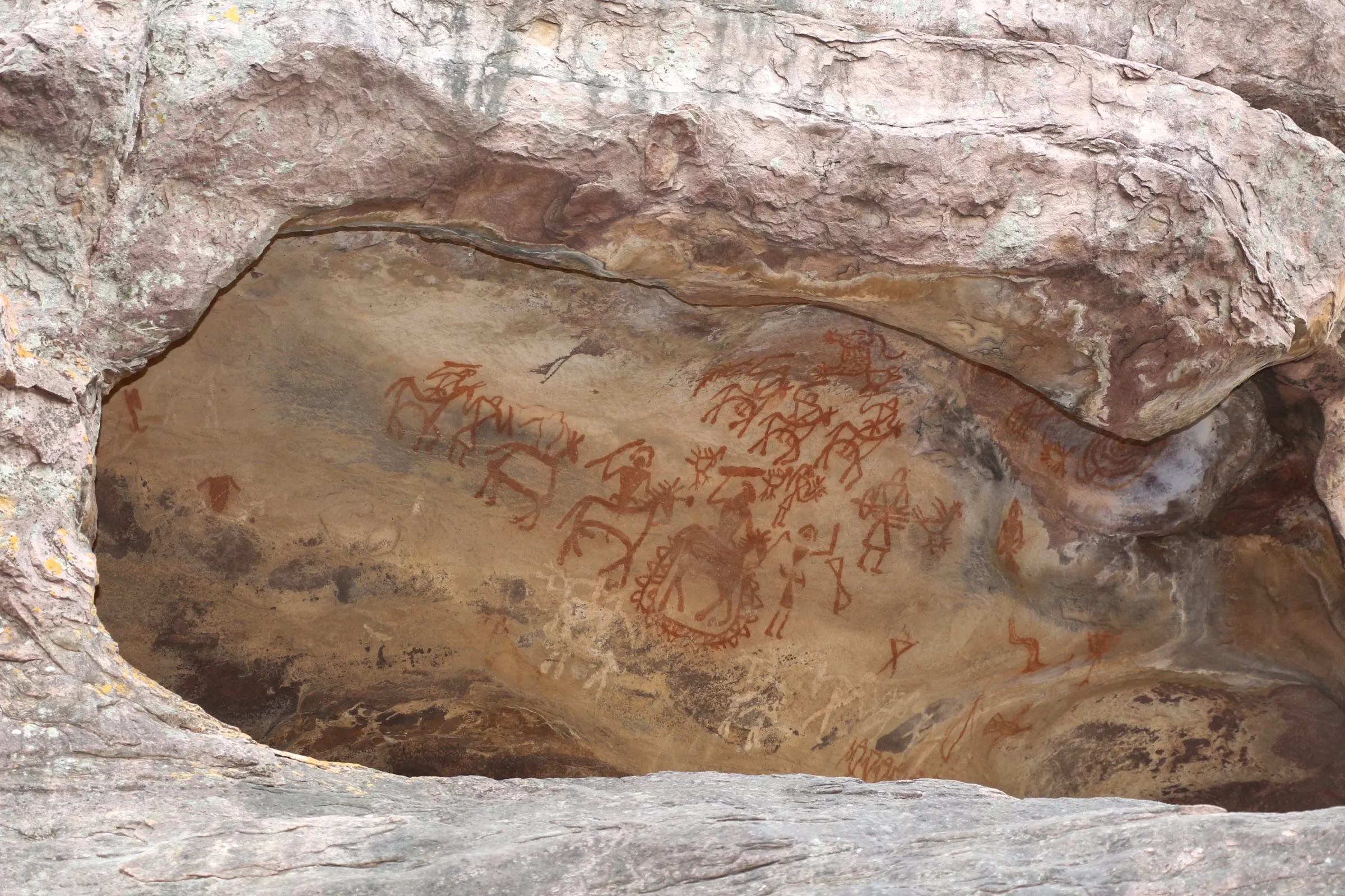 A huge overhanging sandstone rock shelter at Bhimbetka, with a dark hollow beneath the overhang and trees around its base