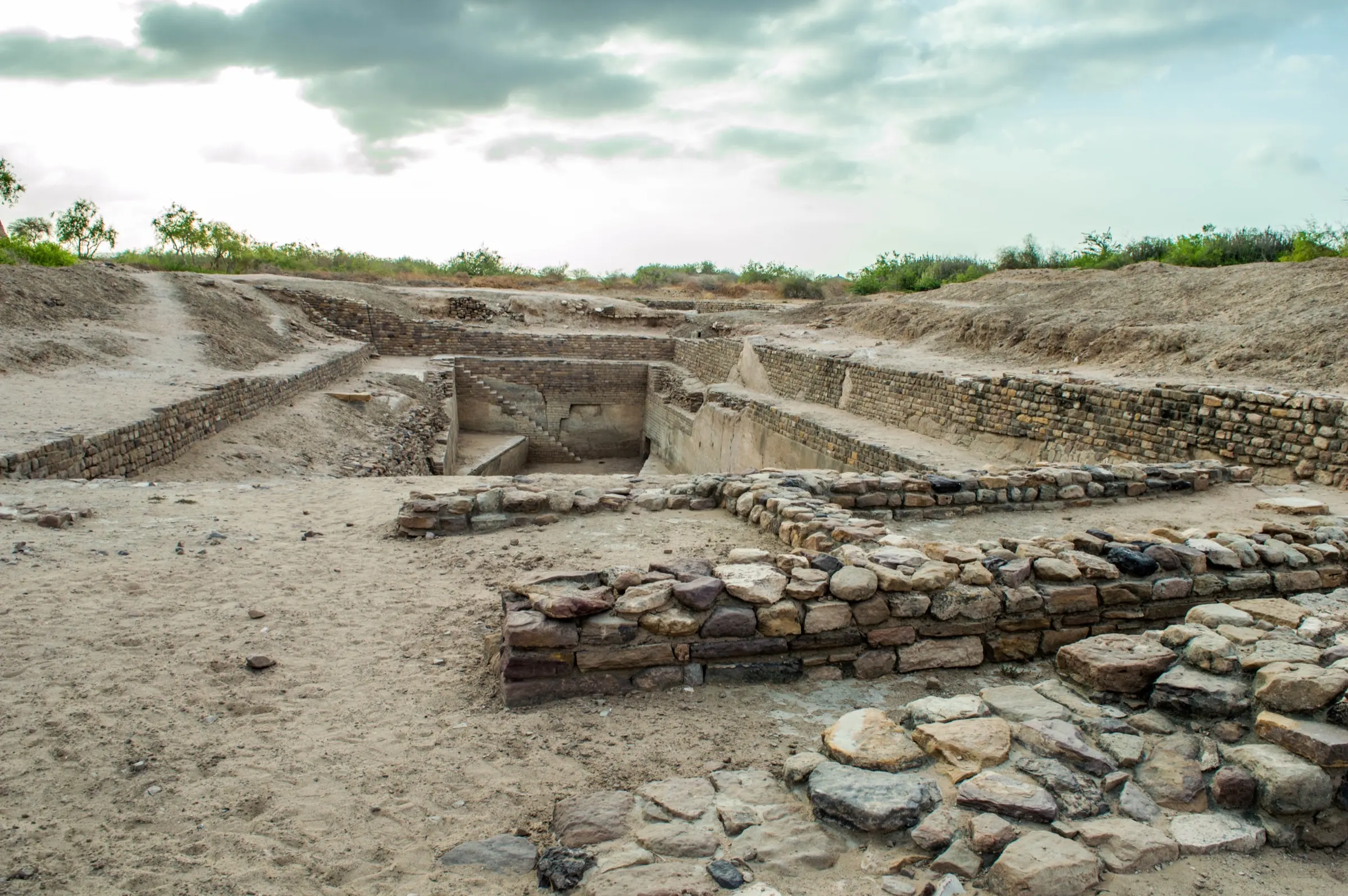 Excavated stone reservoirs and channels at Dholavira, cut deep into the ground in rectangular sections under a pale sky
