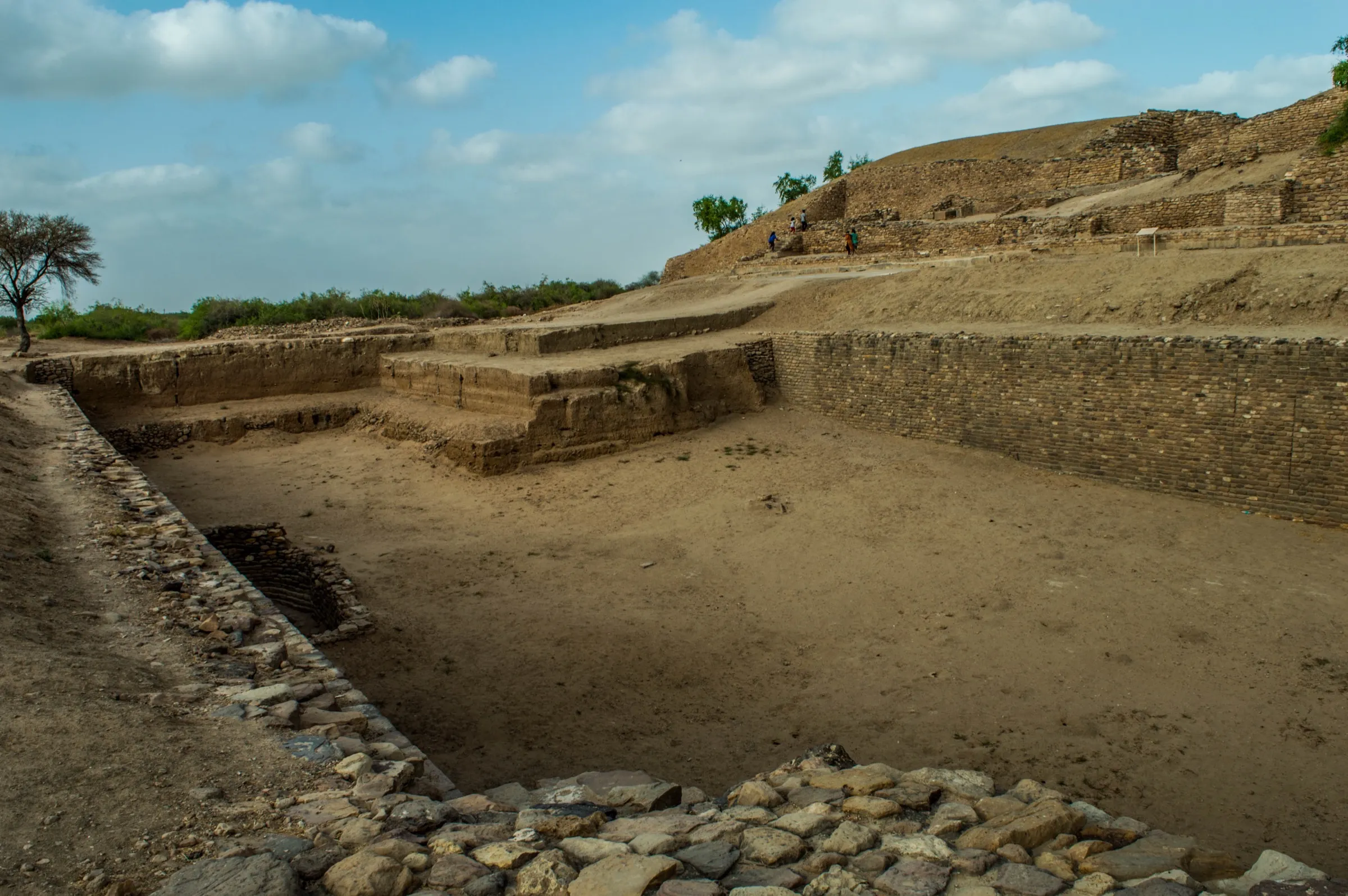 A deep rectangular reservoir cut into stone with stepped sides at the excavated site of Dholavira, under a clear sky