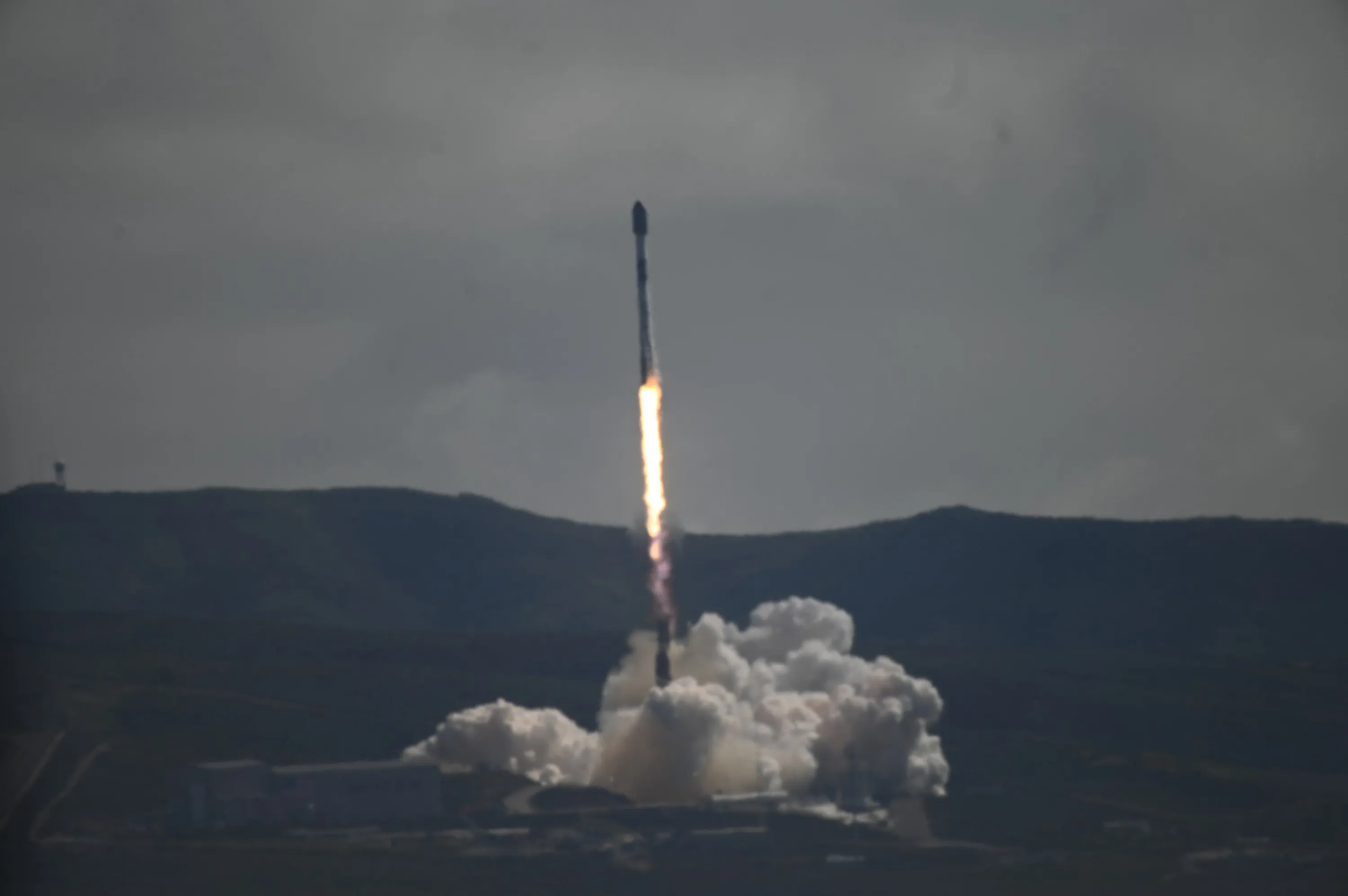 A Falcon 9 rocket rising on a column of flame and smoke from a launch pad