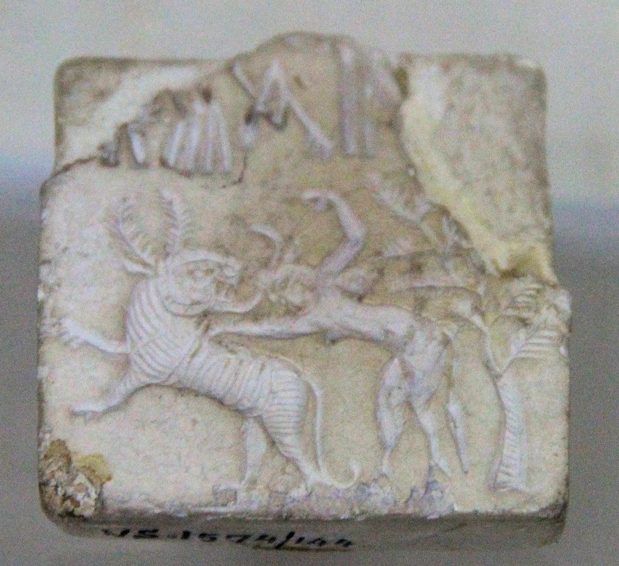 A small square steatite seal carved with figures and a line of Indus script signs