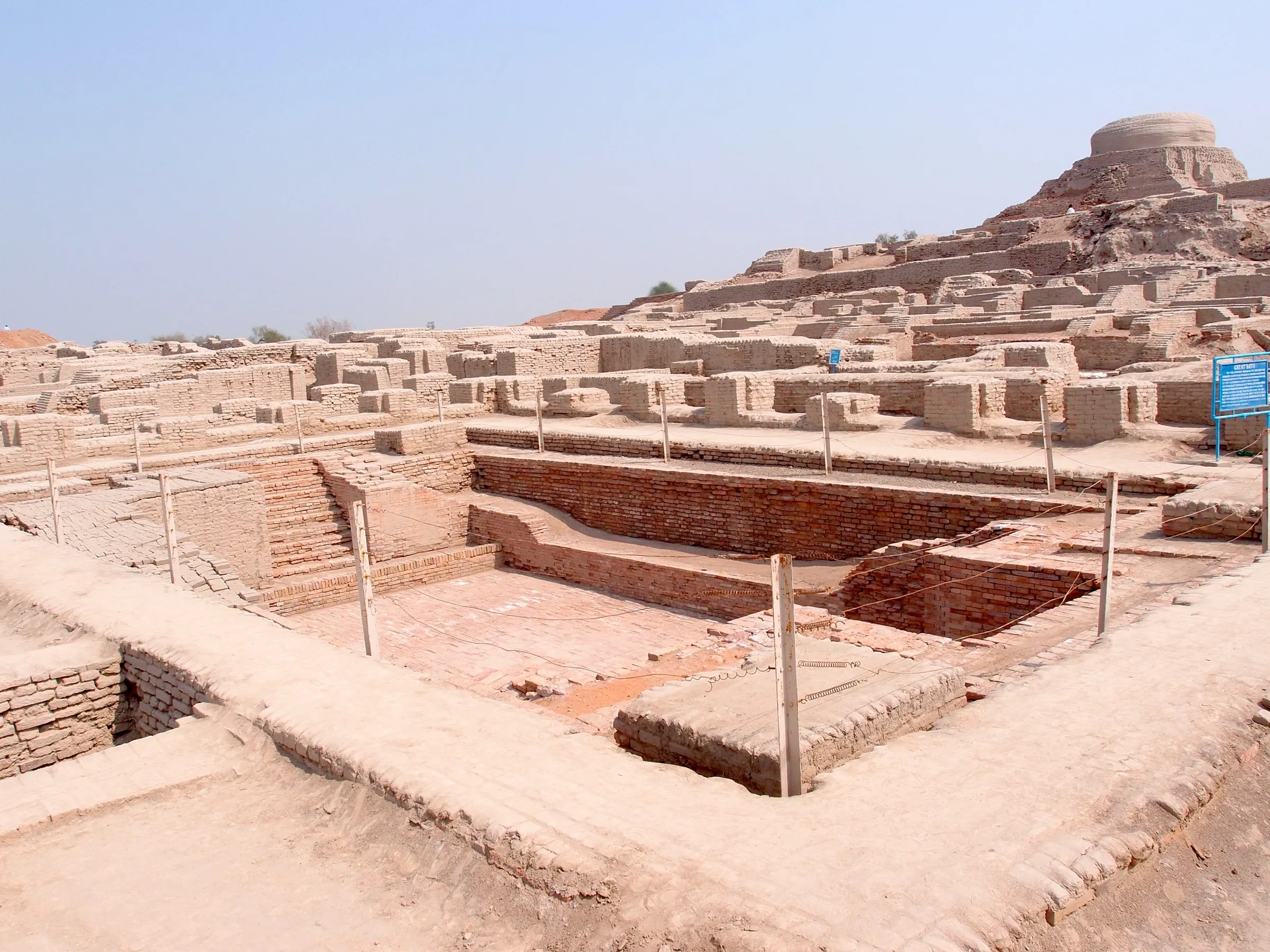 The excavated brick ruins of Mohenjo-daro, with the rectangular Great Bath in the foreground and a raised mound behind