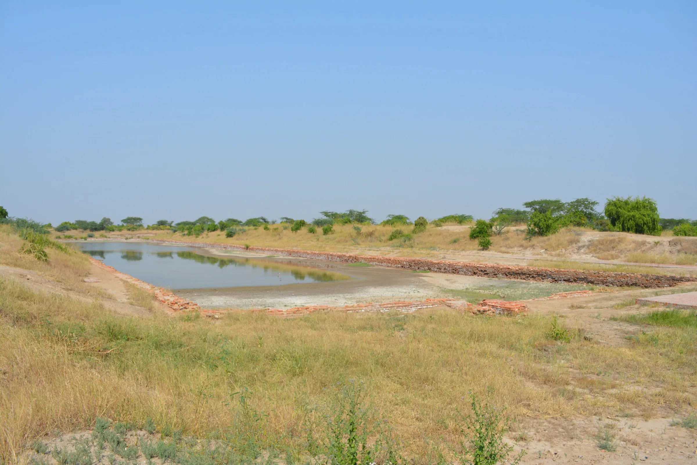 A large rectangular brick-lined basin at Lothal, with low brick walls along its edges and flat ground beyond