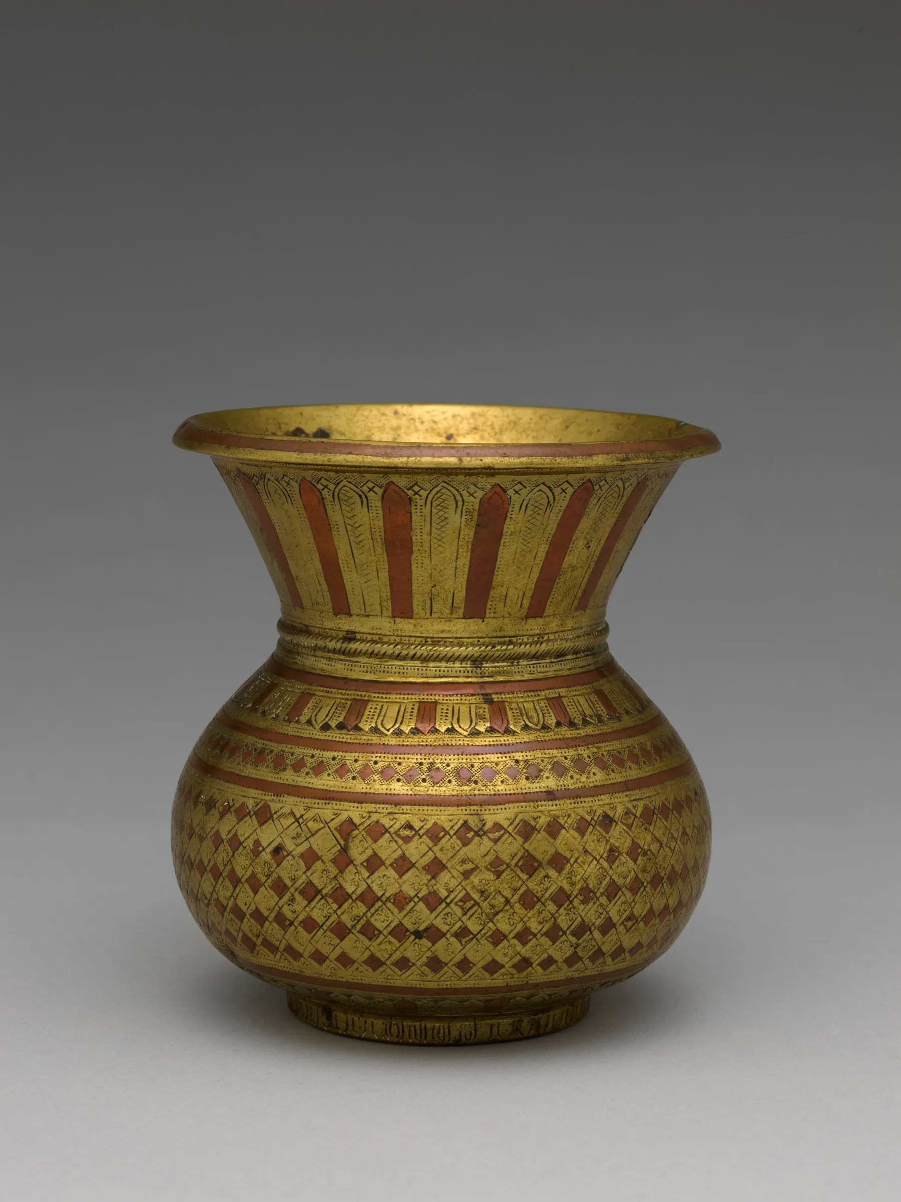 A round-bellied Indian brass and copper water pot, a lota, with a narrow neck and flared rim, against a plain background