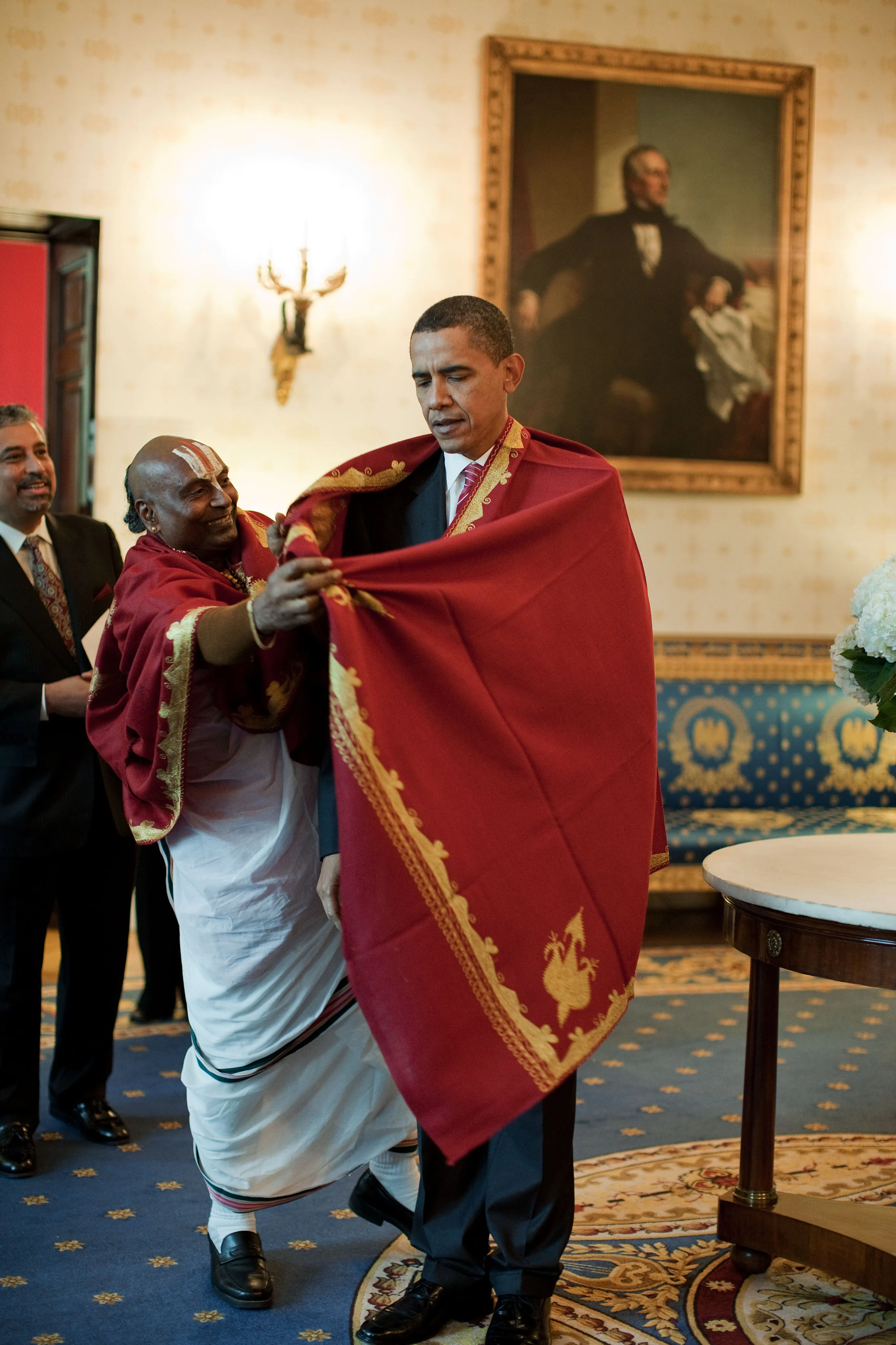 Barack Obama receiving a red shawl from a Hindu priest in the Blue Room of the White House