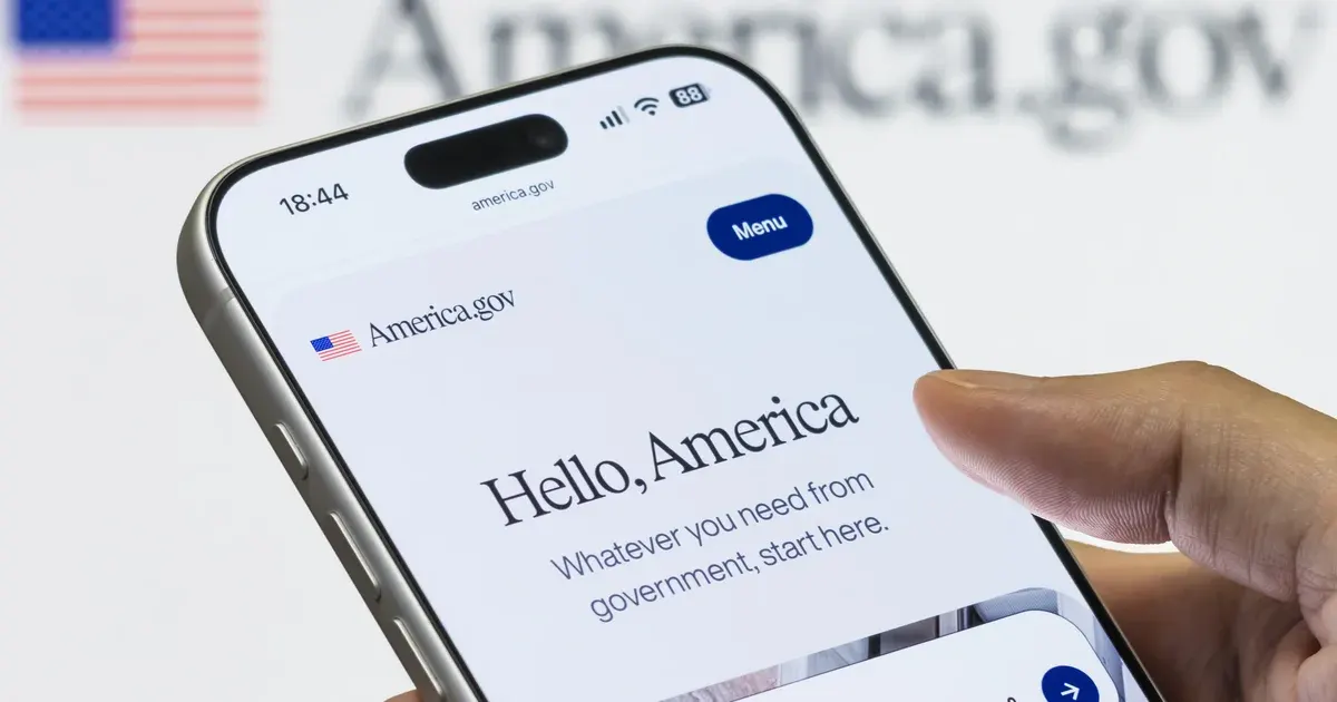 A hand holds a phone open at America.gov, showing a small American flag, the words Hello, America and the line Whatever you need from government, start here