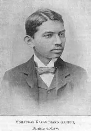 A head-and-shoulders photograph of the young Gandhi in a dark suit, high collar and tie, with short hair
