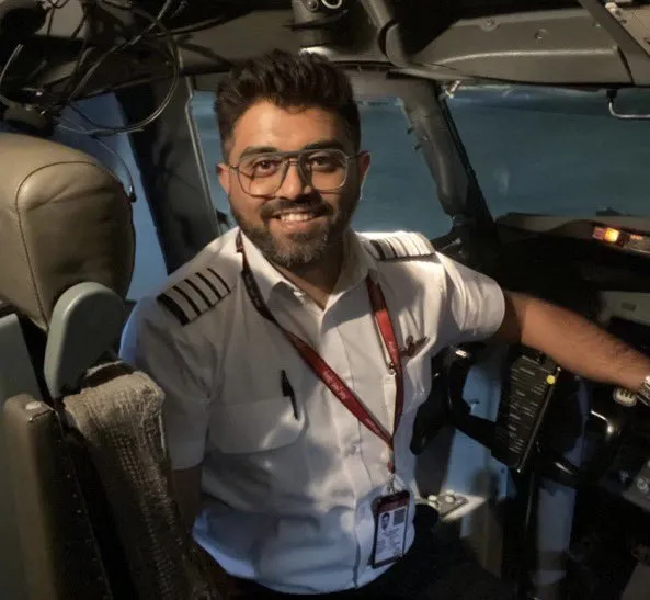 Captain Smit Machchhar, smiling, in a white pilot's shirt with four-stripe captain's epaulettes, seated in an airliner cockpit