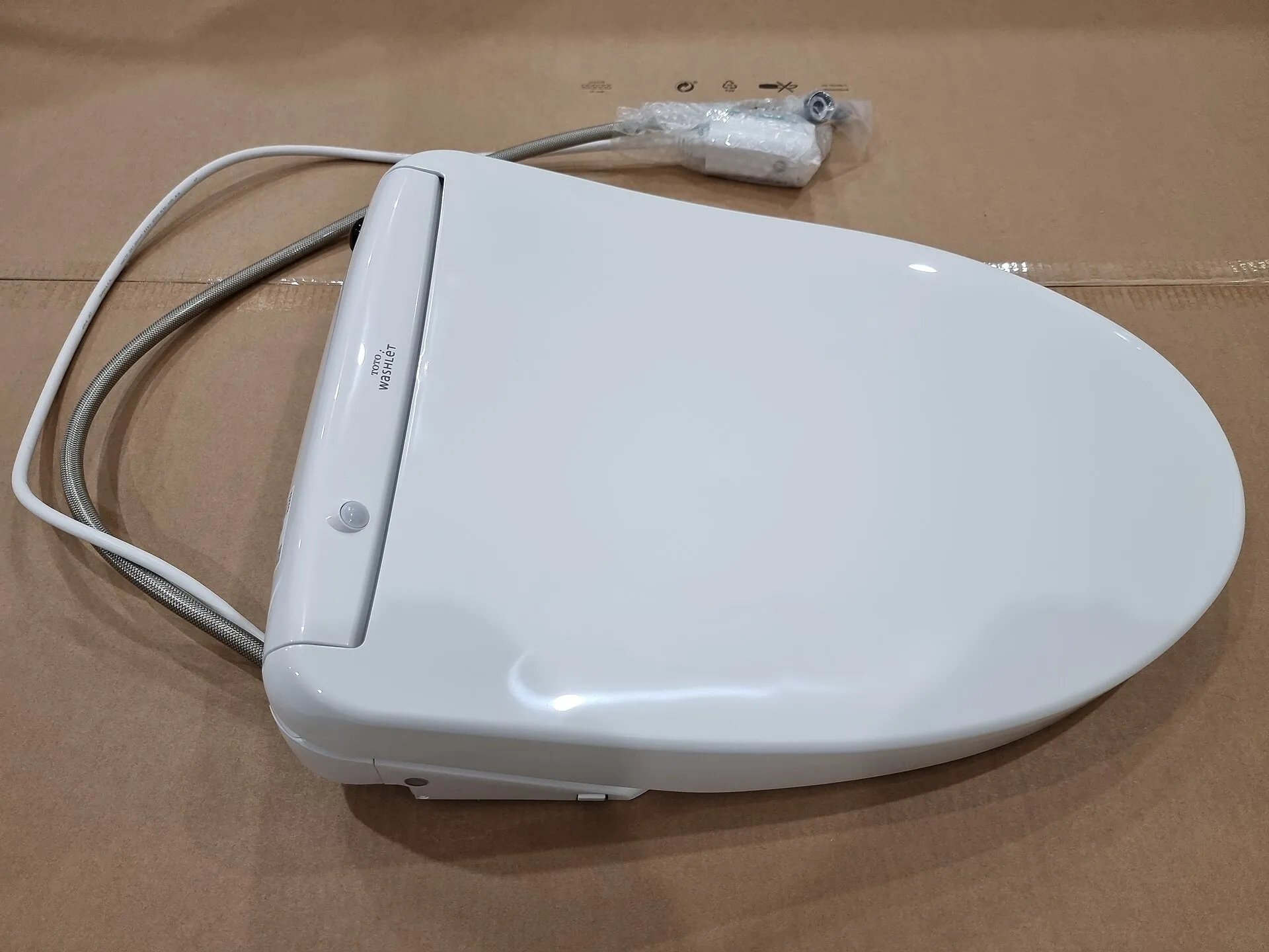 A modern Japanese electronic toilet seat with a control panel at the side, seen from above